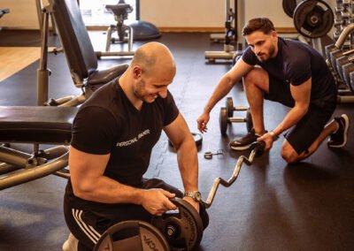 un personal trainer aide son client à charger sa barre avec des disques de poids