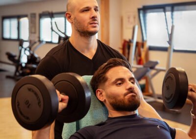 un coach assure son client lors d'un développé militaire aux haltères